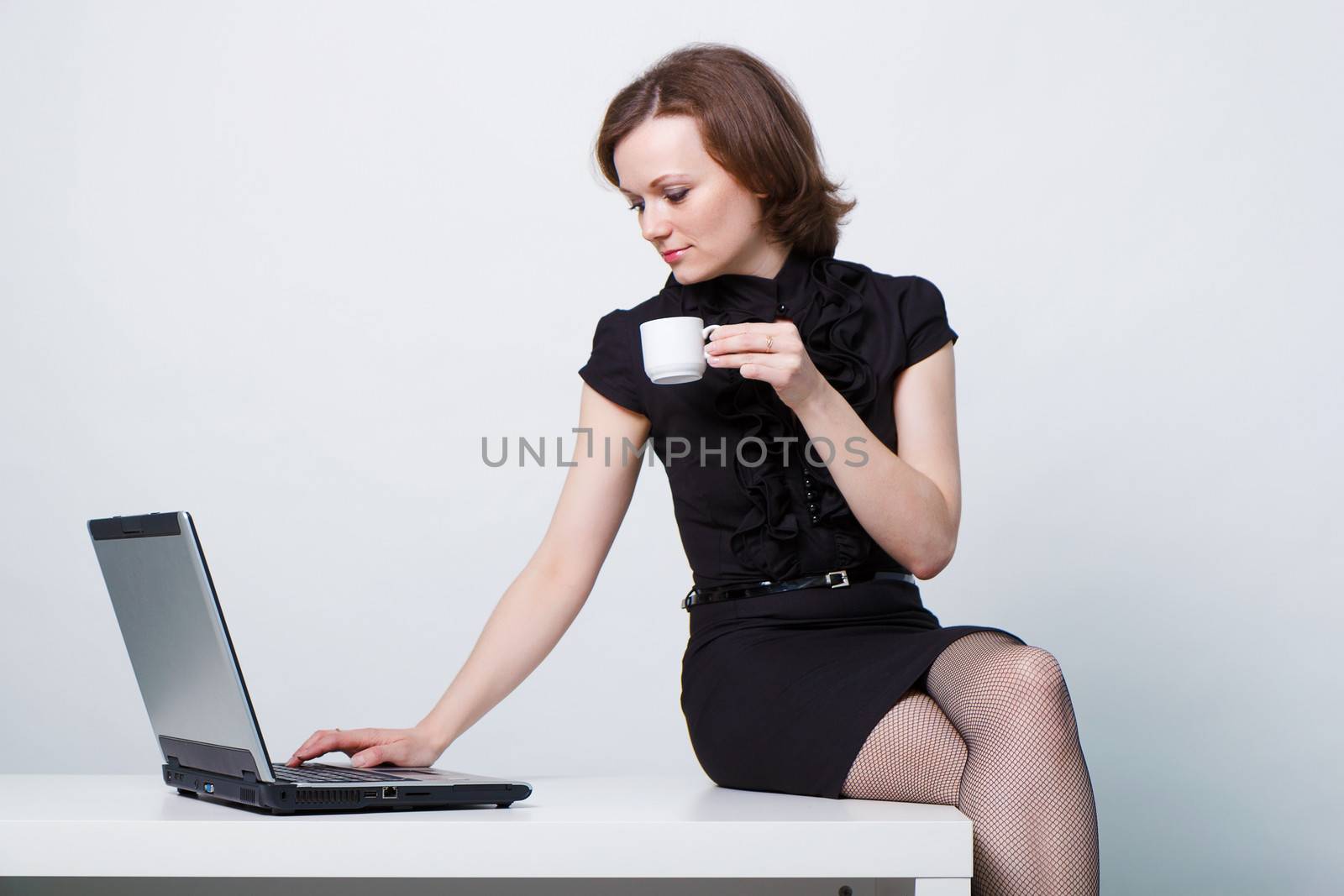 sitting on the table an attractive girl with a laptop and a cup of coffee