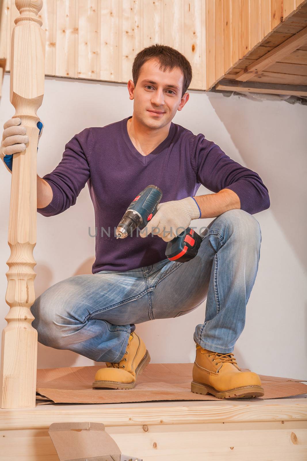 a young carpenter sitting and holding cordless drill by mihalec