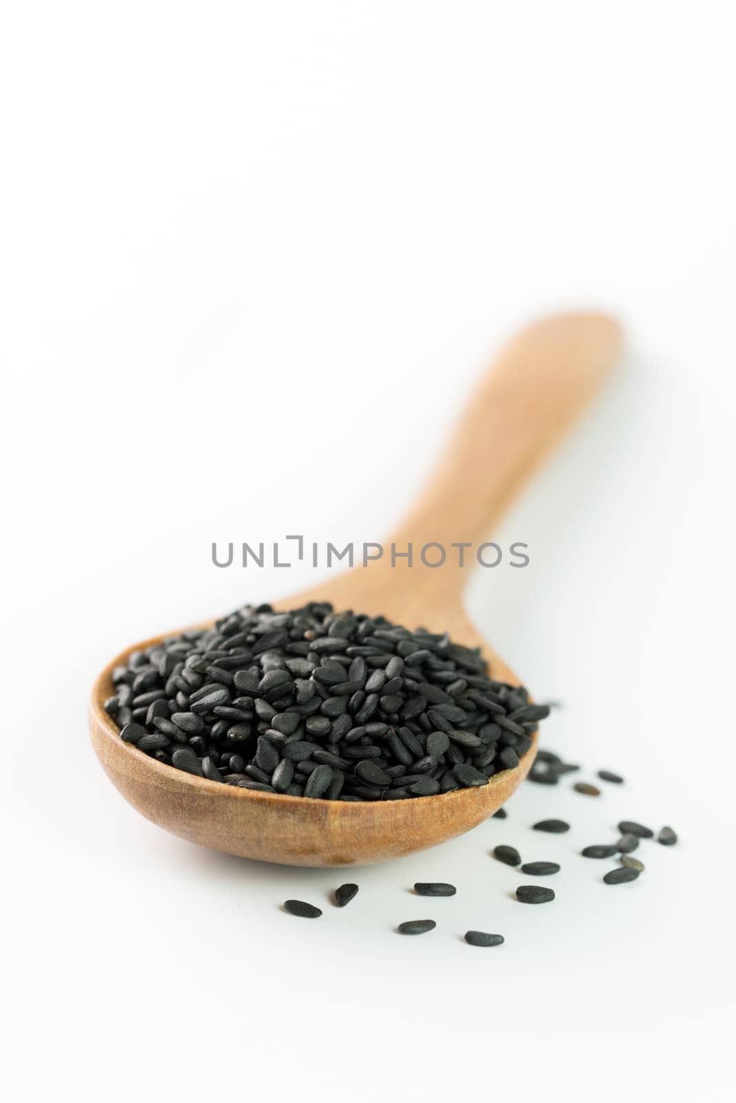 Heap of black sesame on wooden spoon on white background