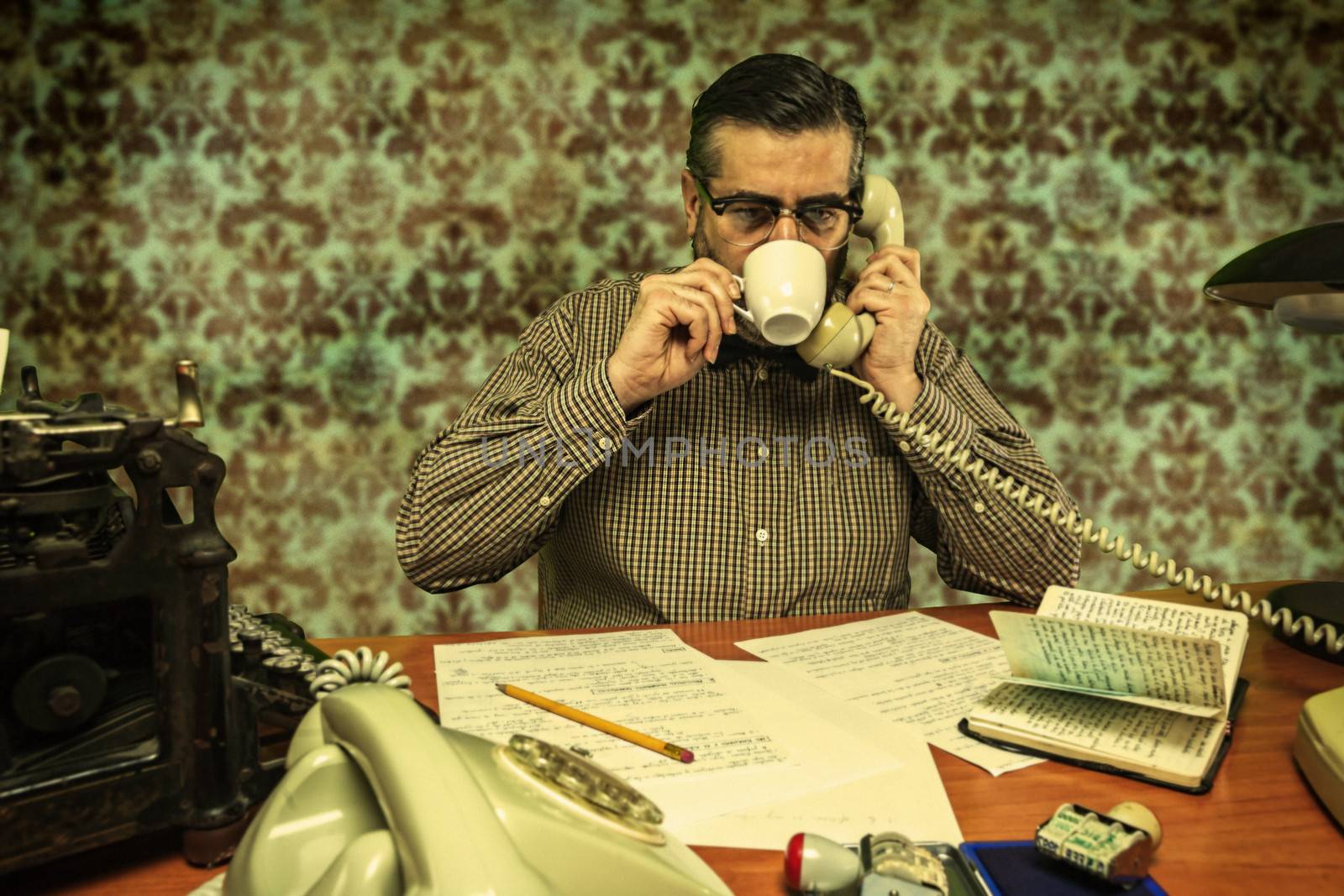 Office employee with glasses sipping coffee while talking on the phone in the 1960s