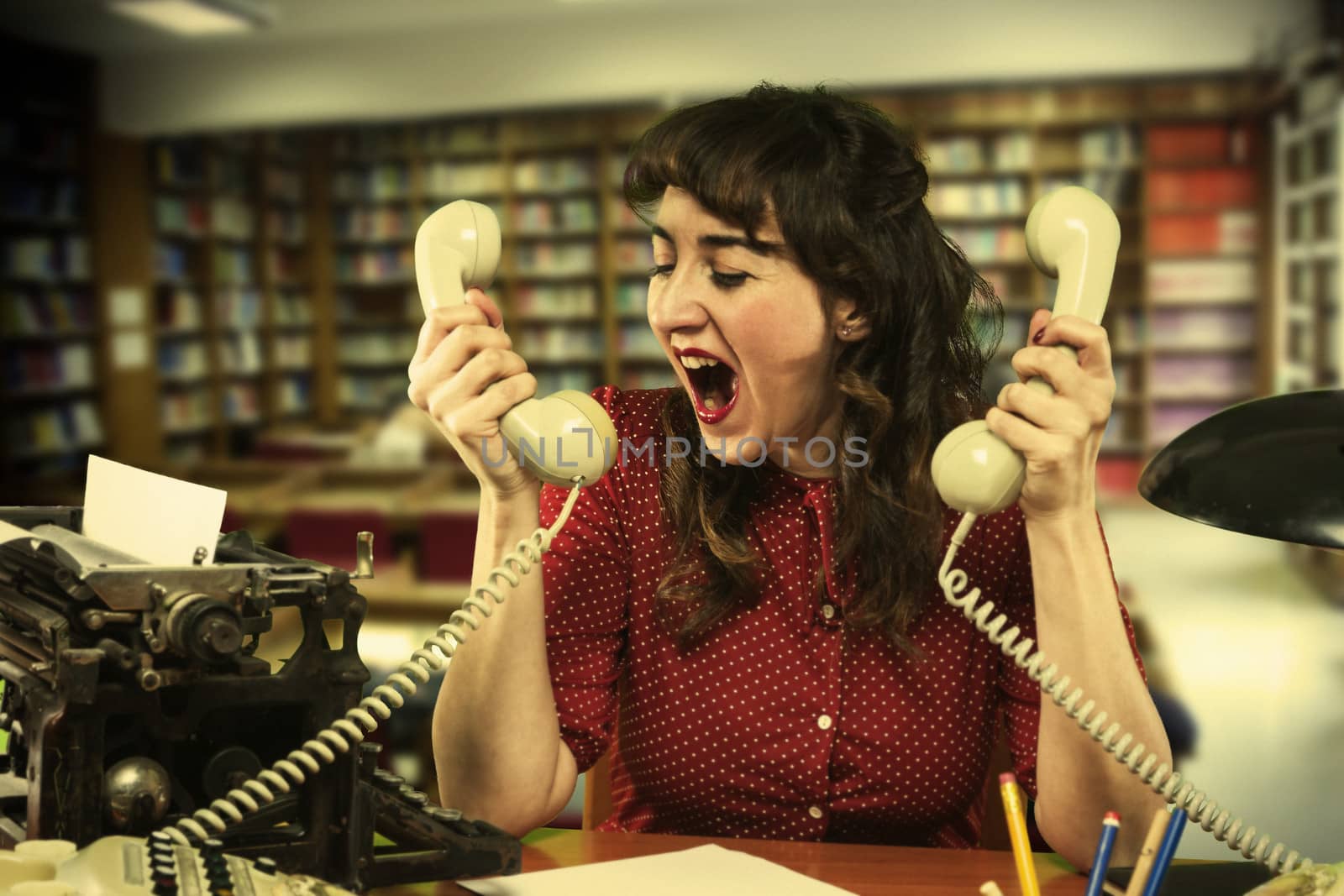 Young woman with red dress desperate with two telephones in both hands in office, 1960's