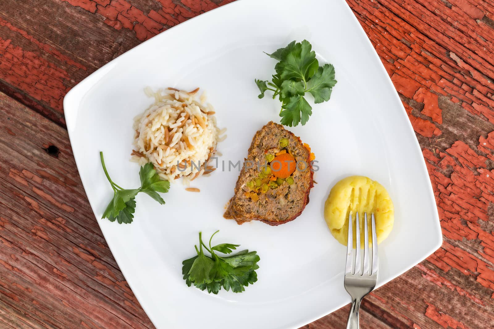 Vegetable stuffed meatloaf served with rice pilaf and mashed potato, garnished with parsley on picnic table