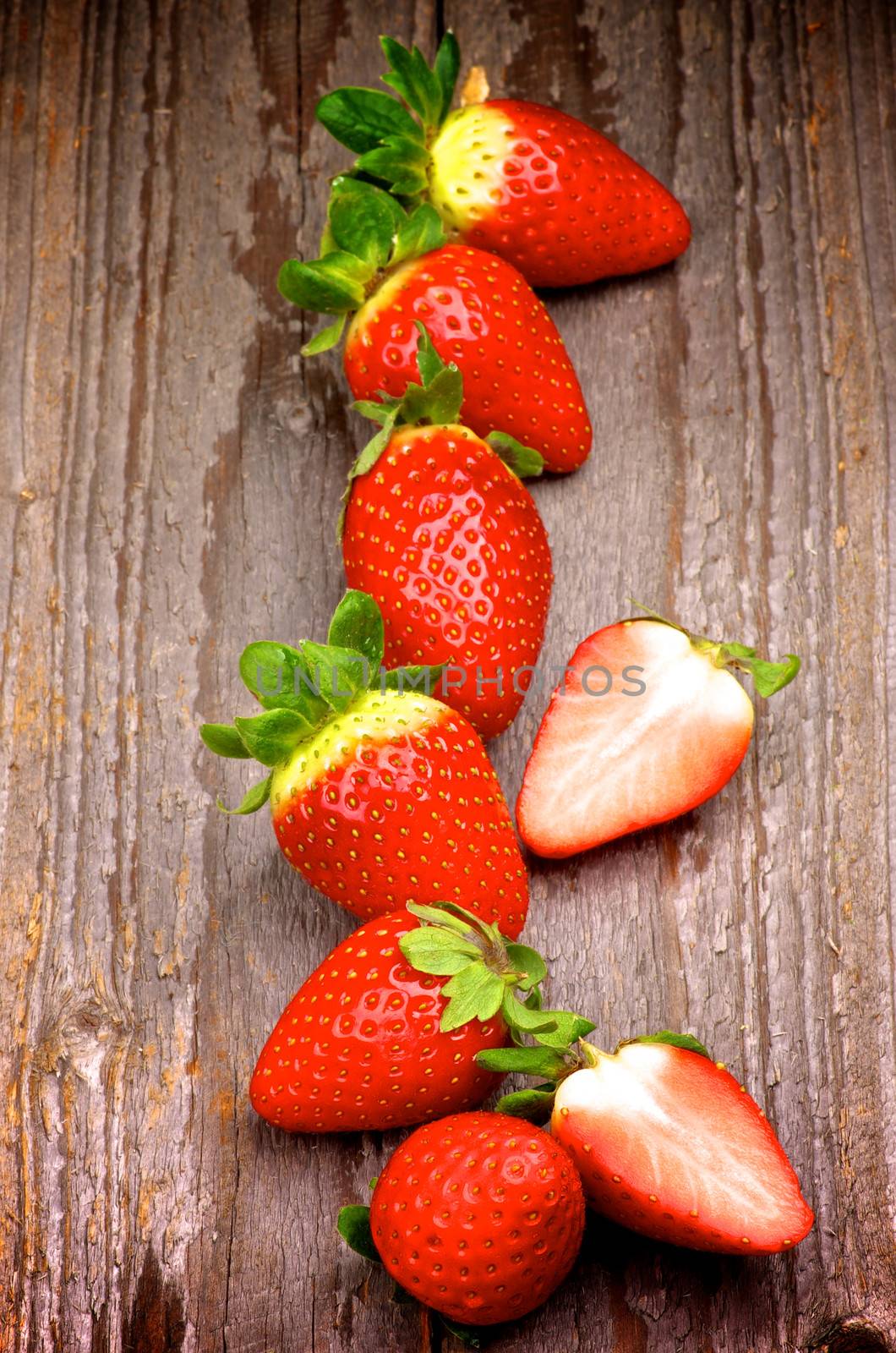 Fresh Ripe Strawberries Full Body In a Row and Halves isolated on Rustic Wooden background