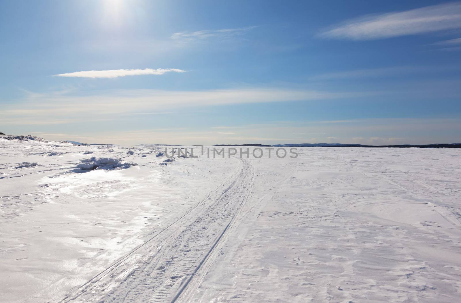Snowmobile trail stretching into the distance against the blue sky and snowy expanses of Russia. Kandalaksha Bay of the White Sea. 