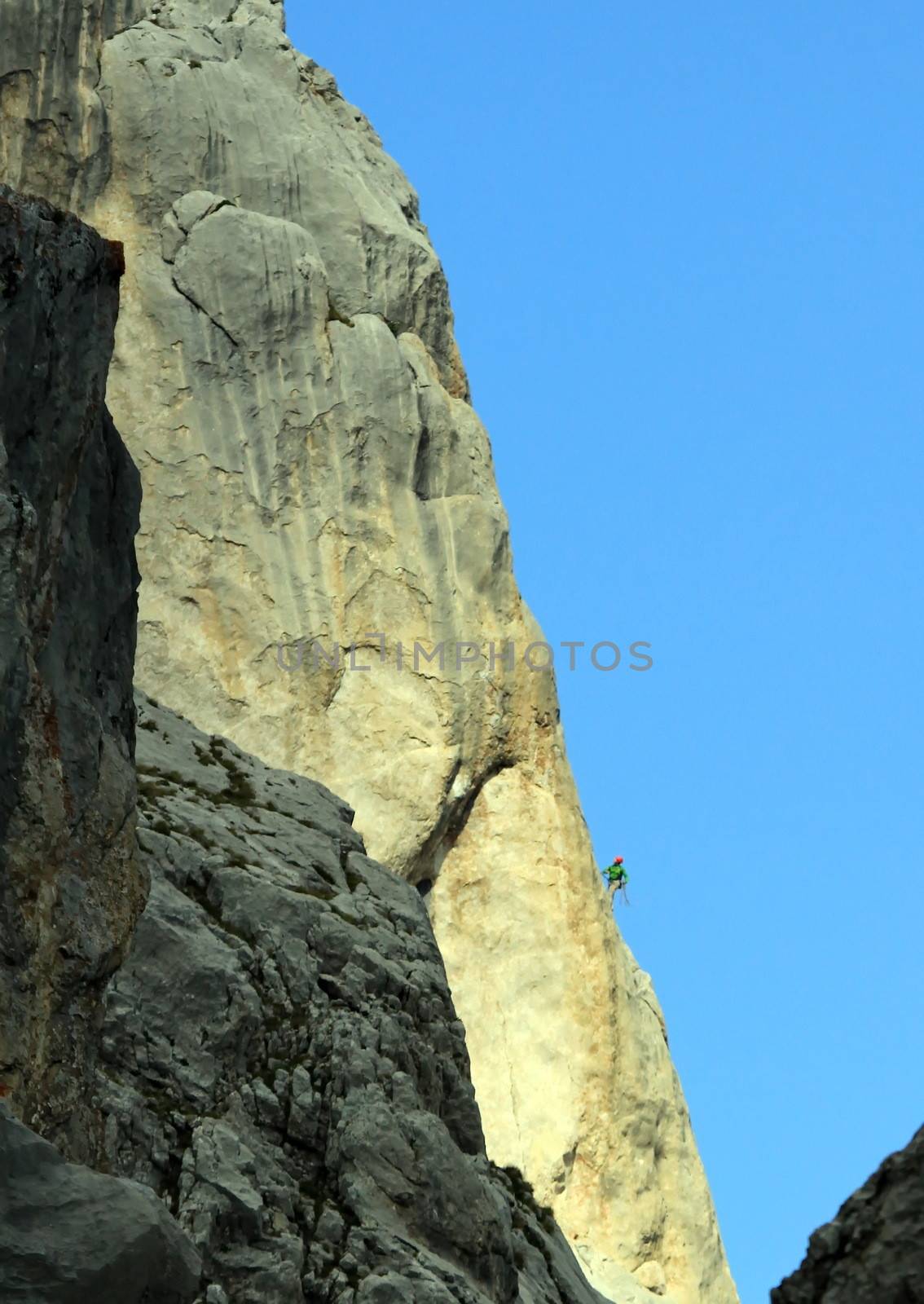 Small climber on a very big mountain rock by sunset light