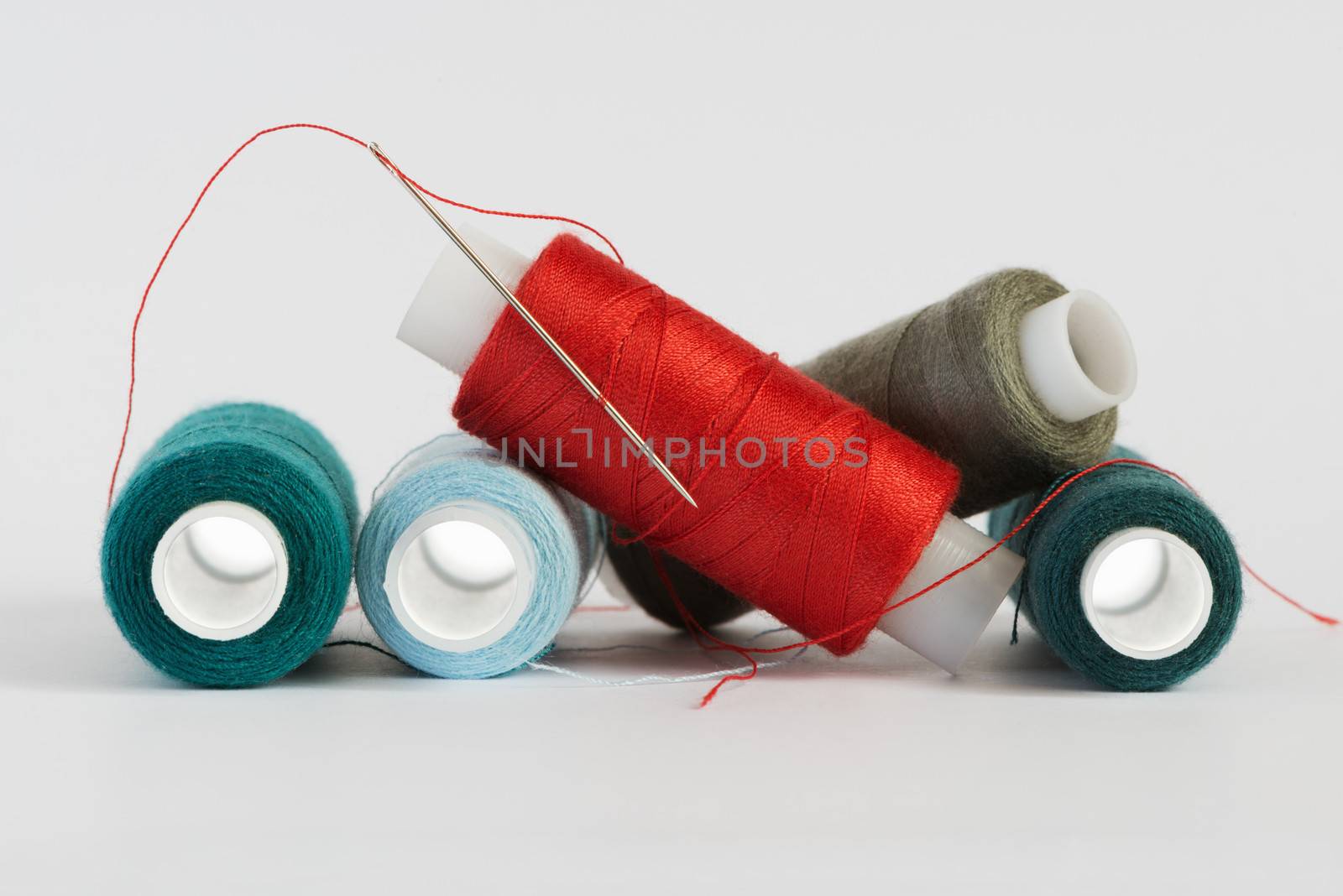 Coils of color threads and steel needle with a red thread