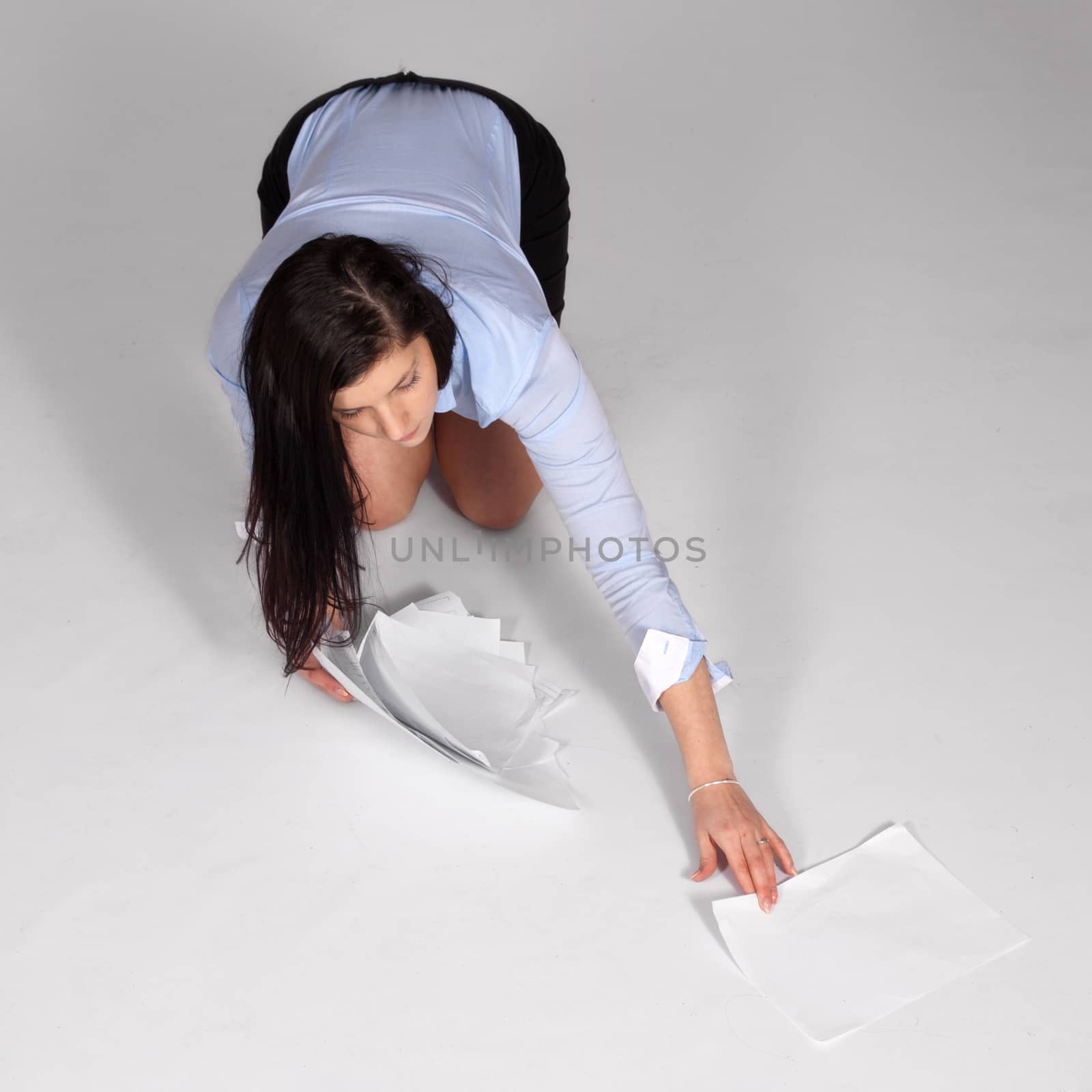 Young woman in mini skirt and blouse, on her knees raised from the ground fallen documents