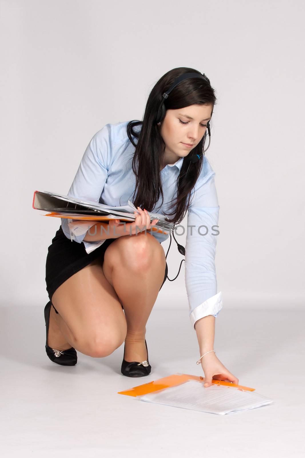 Young woman in mini skirt and blouse, squatting rises from the ground fallen documents  and in addition she call up