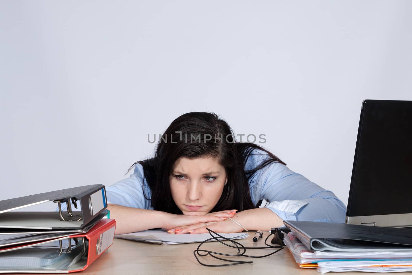 Young woman at the table helplessly looking at the pile of documents