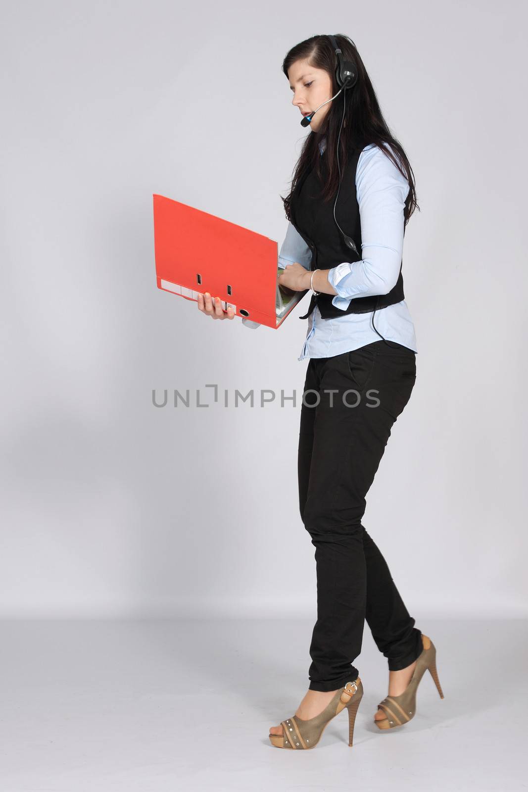 Young woman with headset phone while walking and holding hands a pile of documents