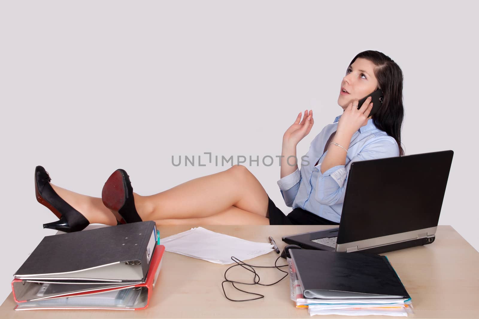 Young female office worker with feet on desk phone and explains