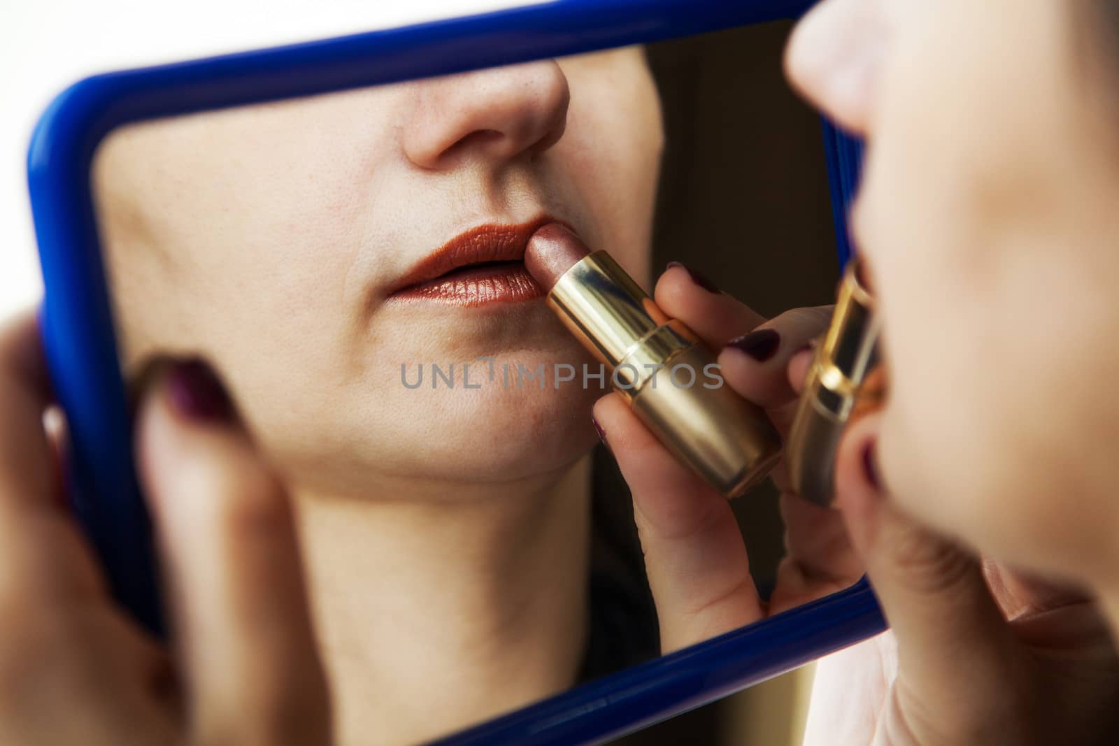 woman paints lips with lipstick before a mirror closeup