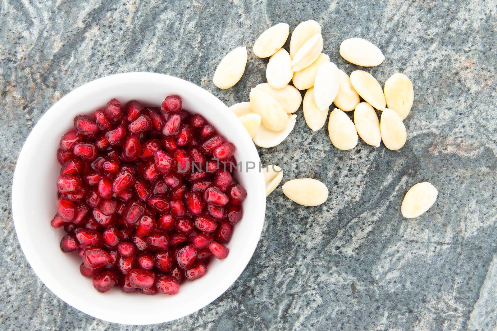 Seeds of fresh pomegranate, next to peeled almonds by coskun