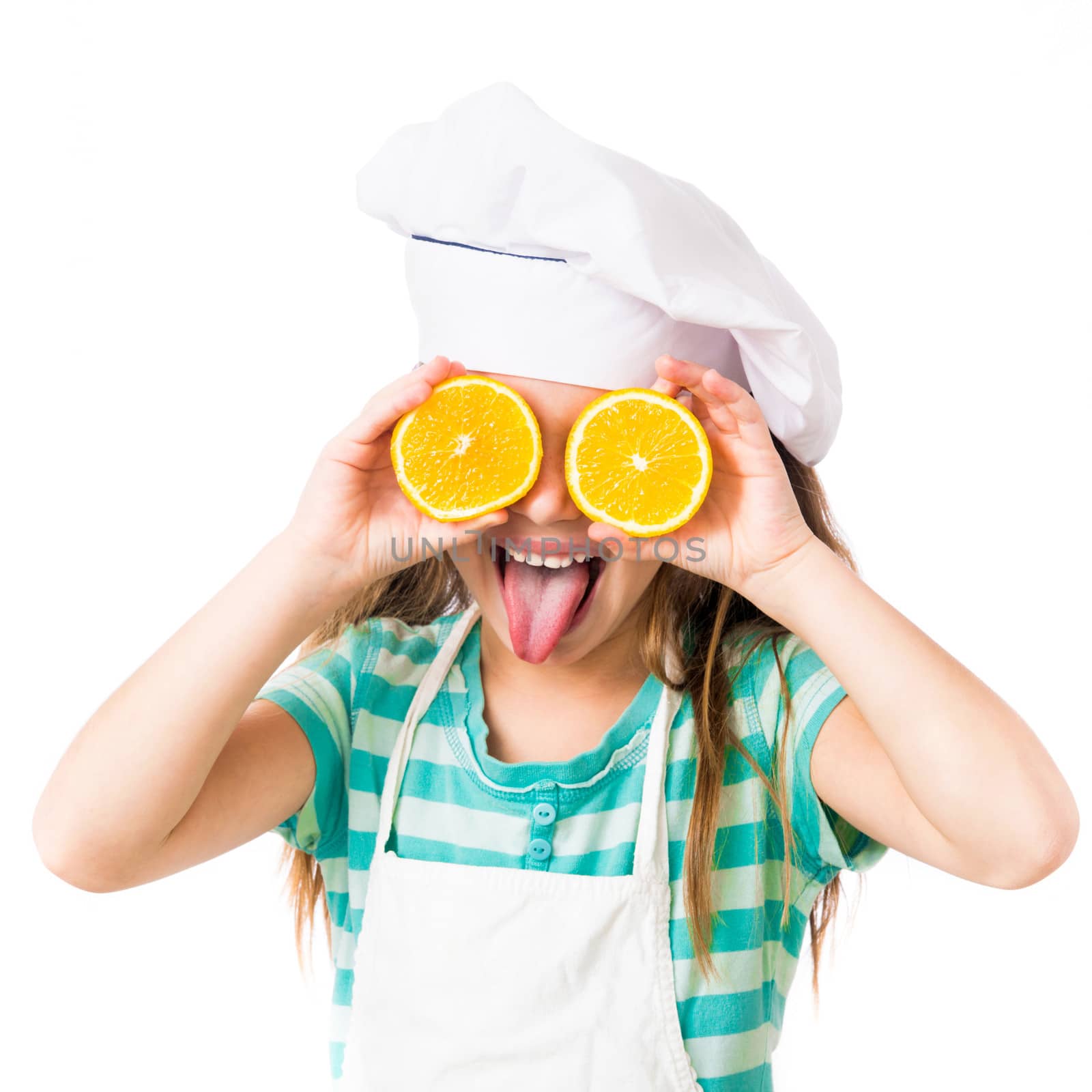little girl in chef hat with two halves of a orange in the eyes shows tongue on a white background