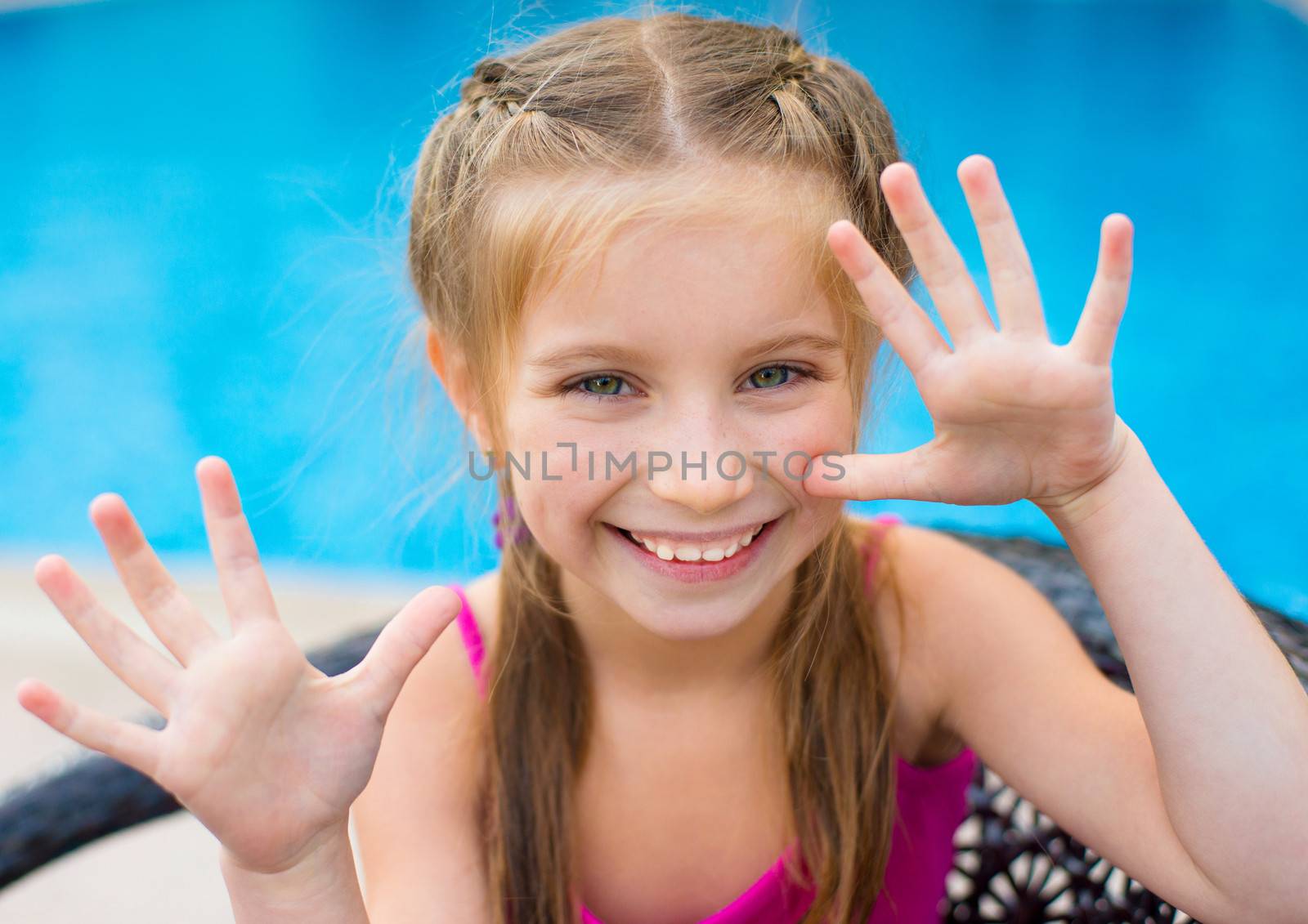 little cute girl holding hands up near a swimming pool