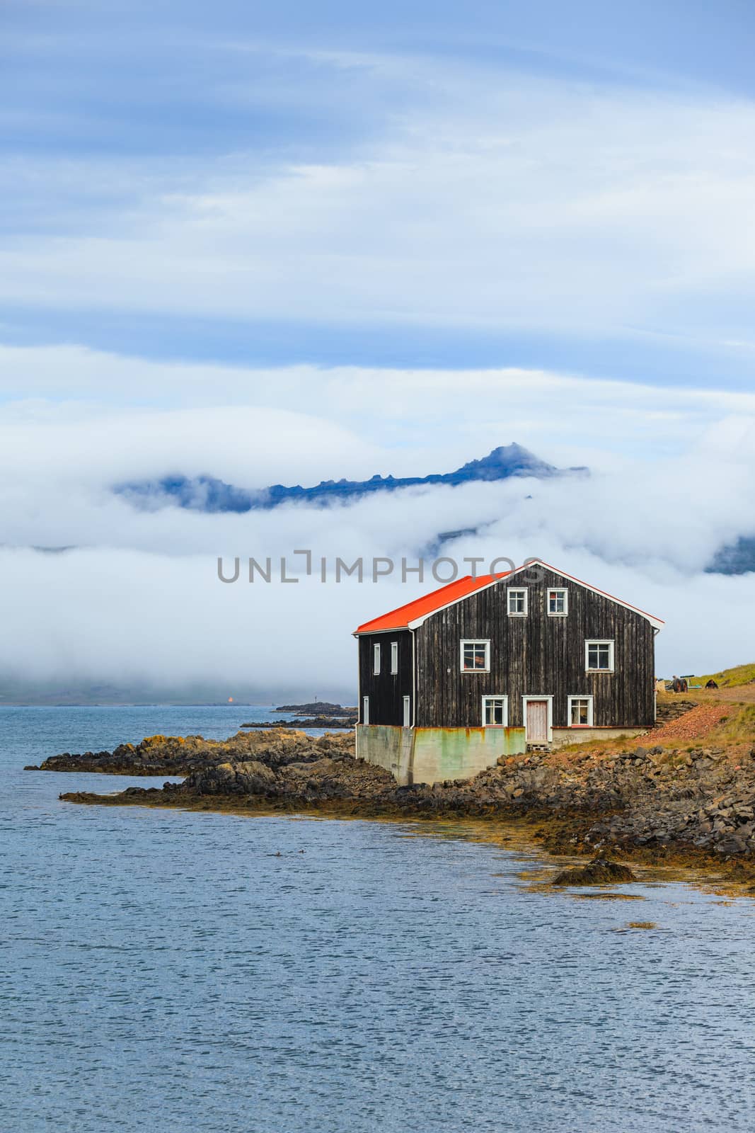 Lonely Black Wooden House at coastline in East Iceland. Vertical view.