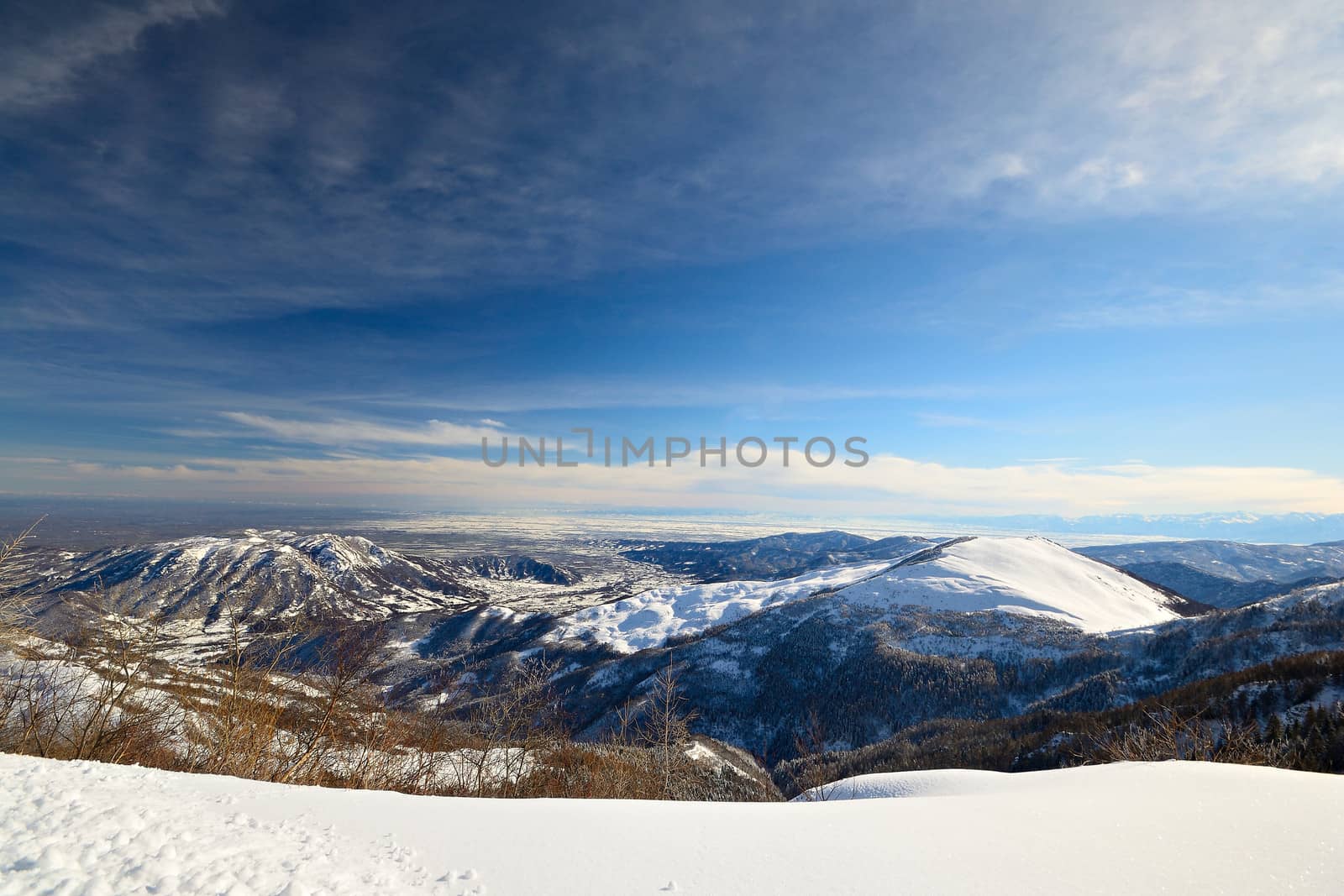 Candid off-piste ski slope in scenic background of mountain peaks, valleys and plain. Piedmont, Italian Alps