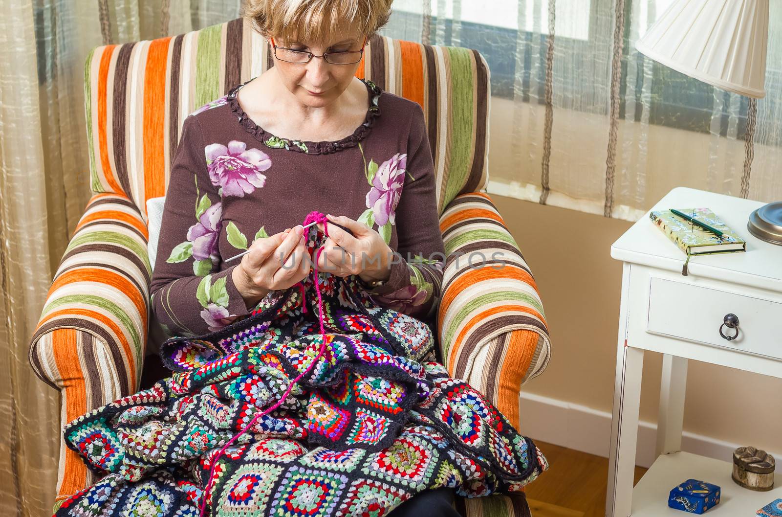 Portrait of senior woman knitting a vintage wool quilt with colorful patches
