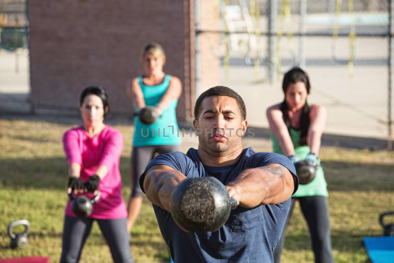 Four people exercising in outdoor boot camp with kettle bells