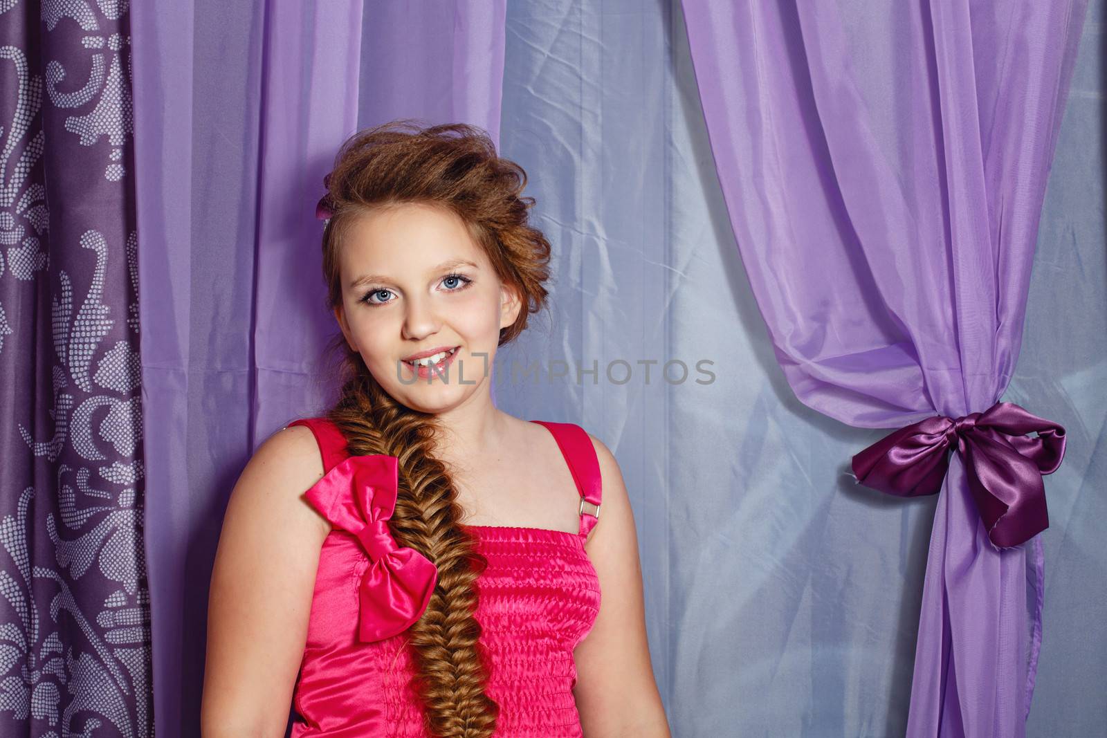Beautiful little girl in a pink dress and braid posing in the interior