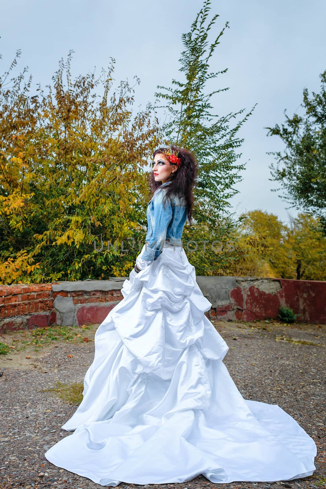 Beautiful bride in wedding dress and denim jacket in autumn park