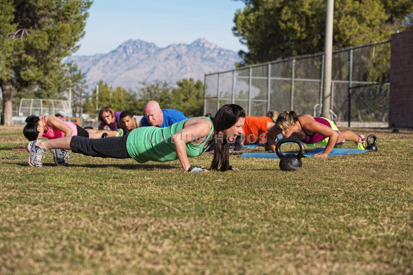 Young woman leading group in push up exercises outdoors