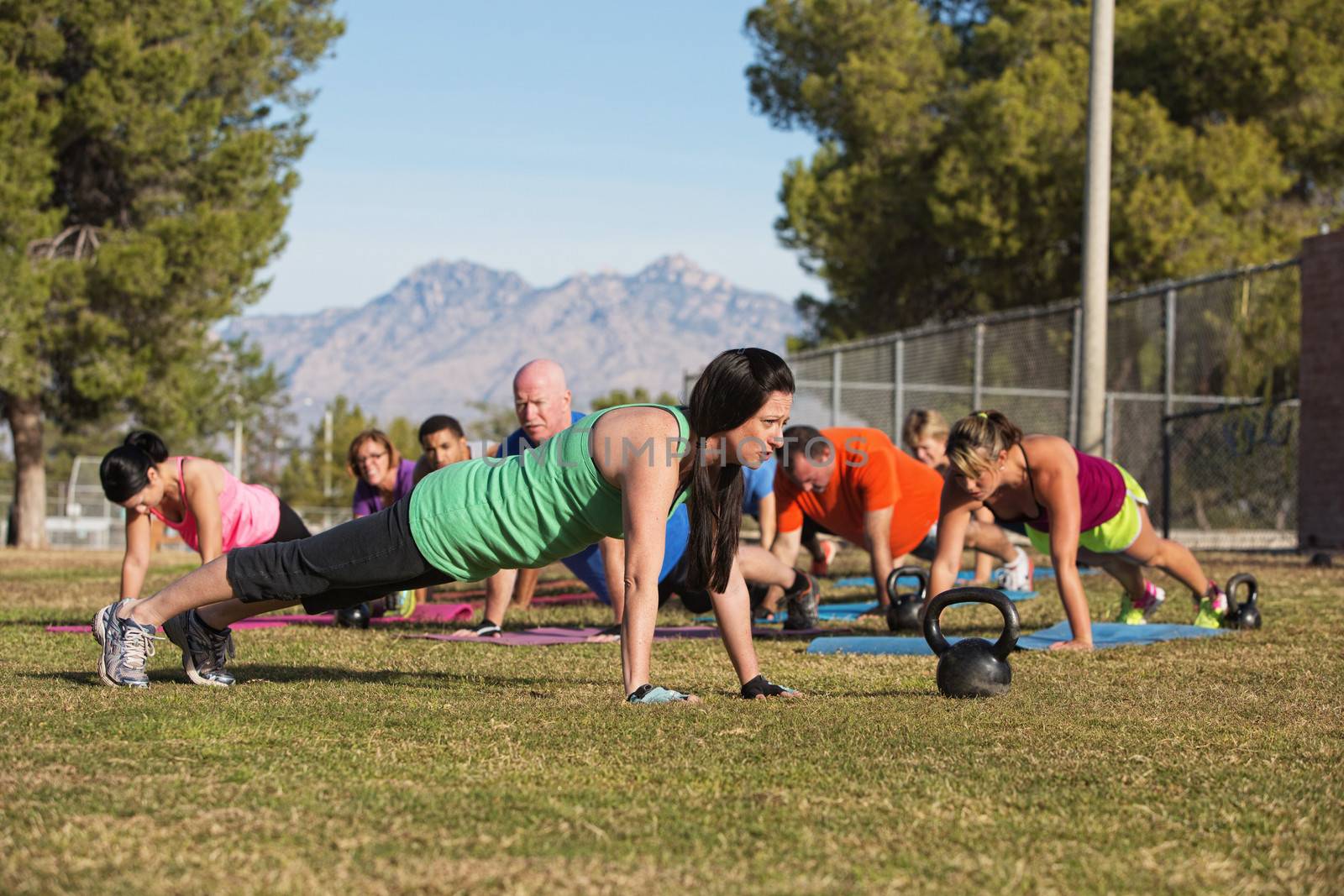 Fitness instructor leading group in push up exercises outdoors