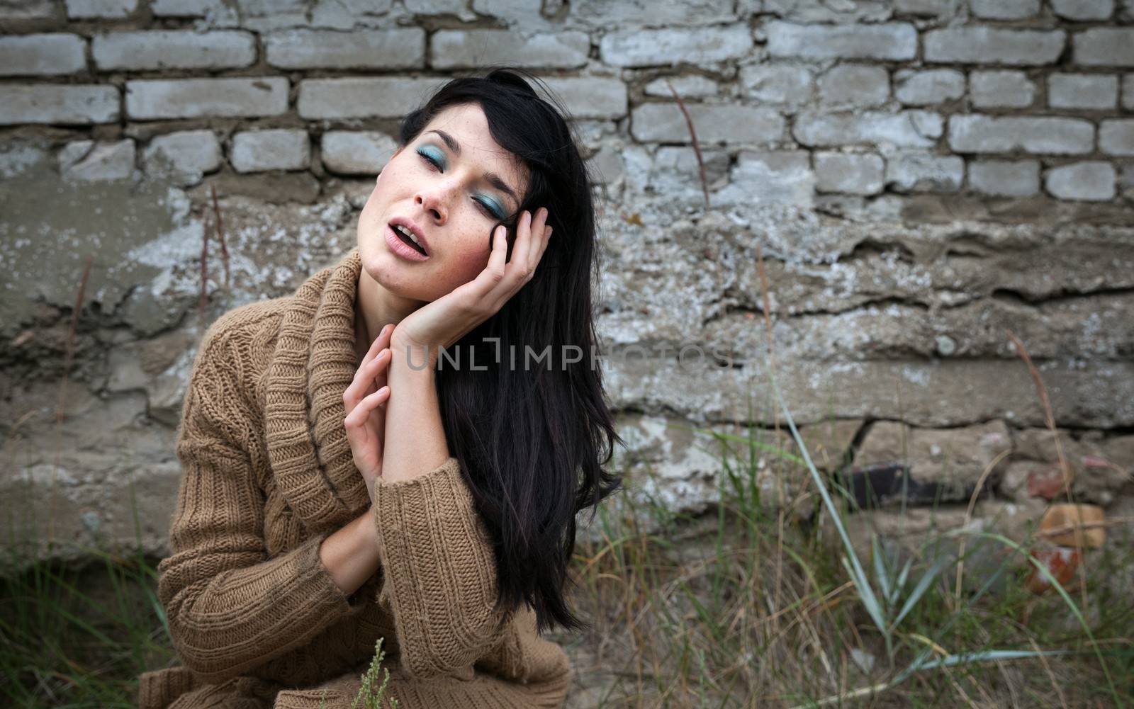 Portrait of a girl with closed eyes against old brick wall