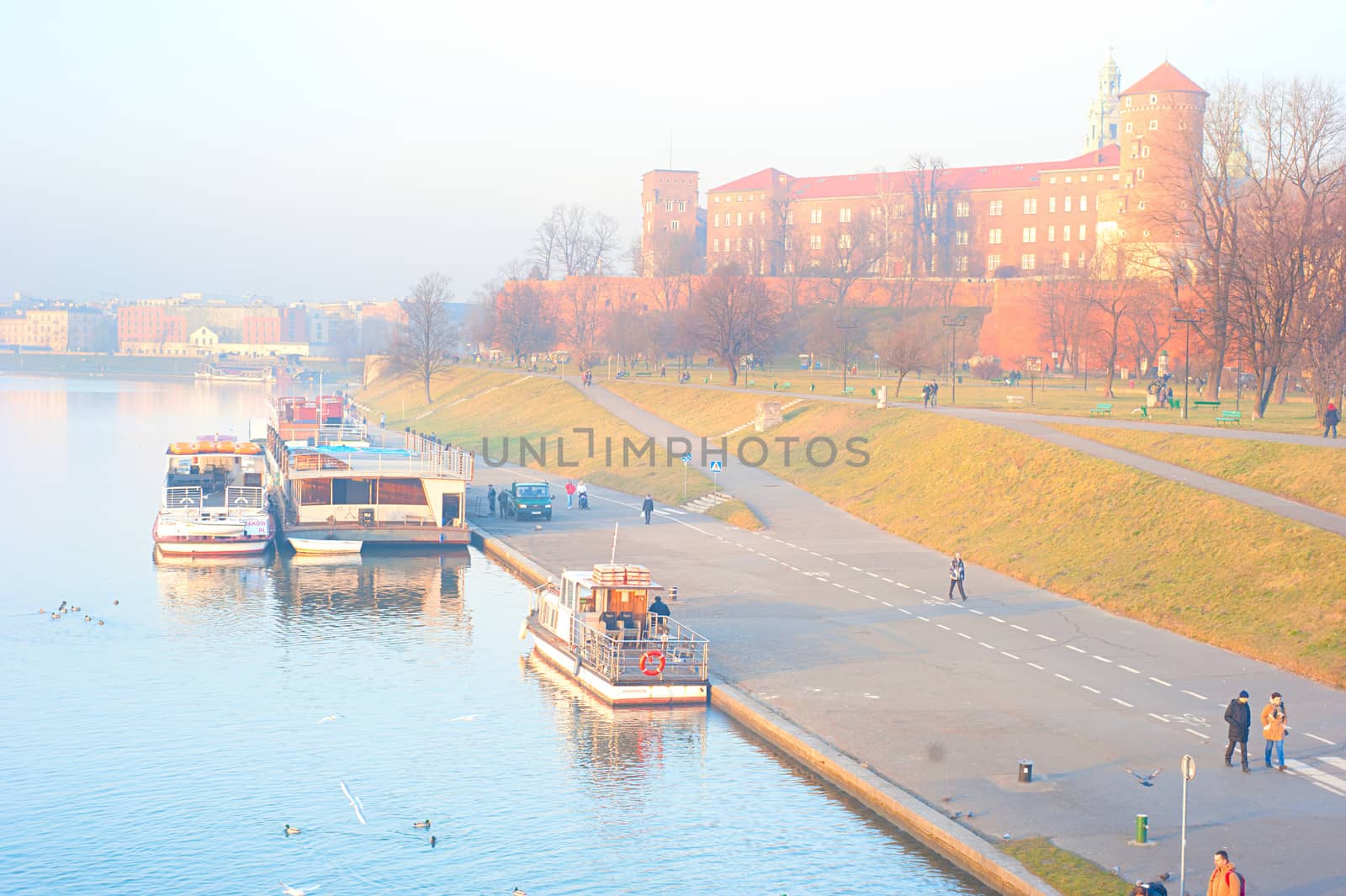 KRAKOW, POLAND - JANUARY 03,2014: People walking on embankment of Vistula river in front of  Wawel castel at sunset.