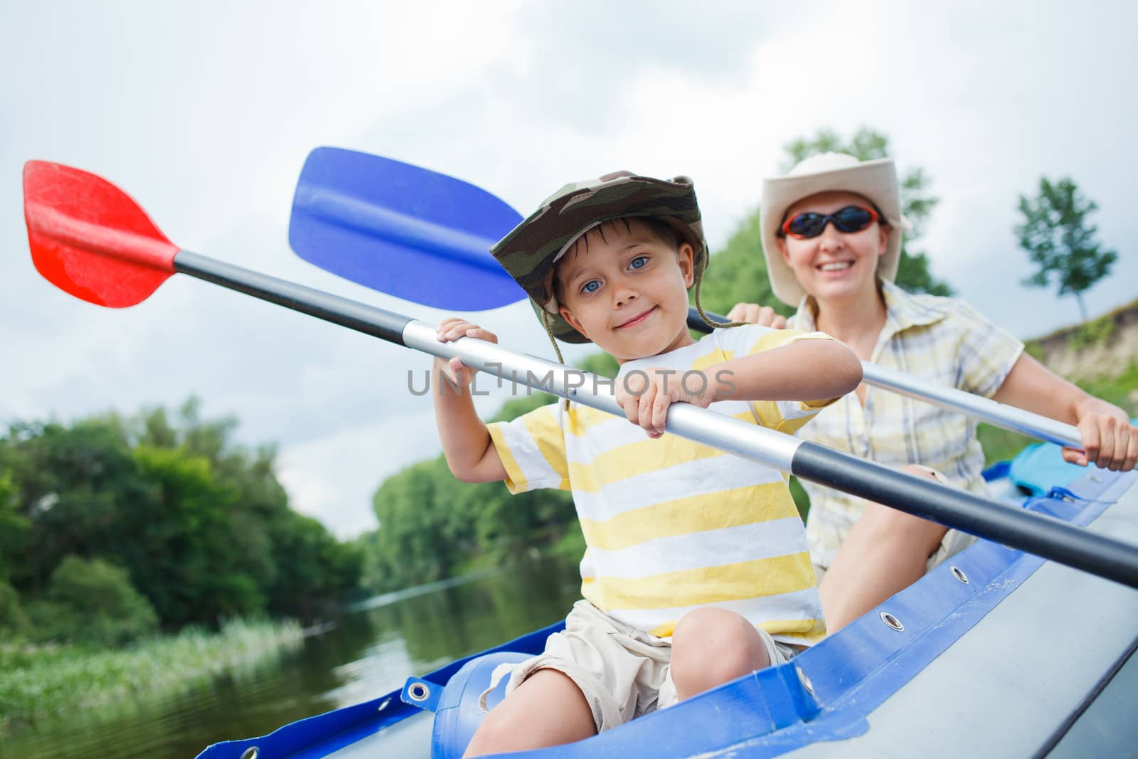 Happy young boy with mother paddling a kayak on the river, enjoying a lovely summer day