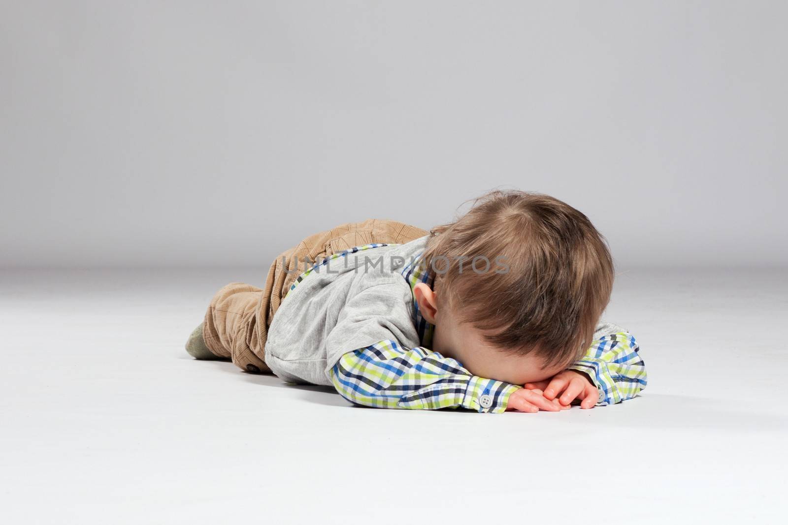 Tired toddler boy lying on the ground with his face down