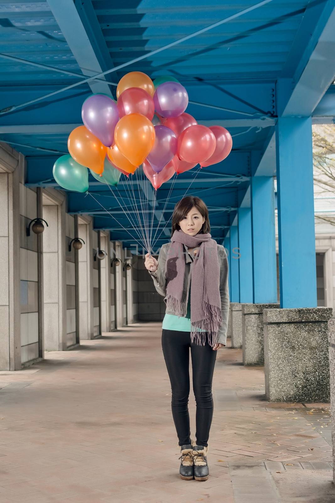 Elegant Asian beauty holding balloons under bridge in city.