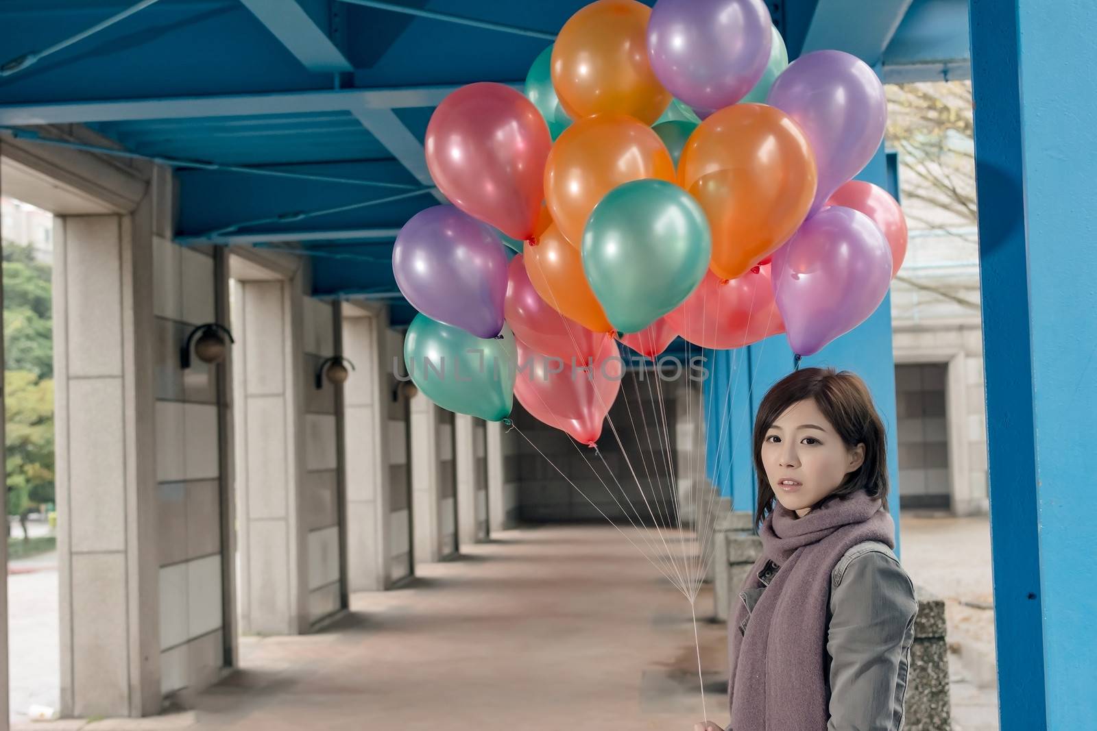 Elegant Asian beauty holding balloons under bridge in city.