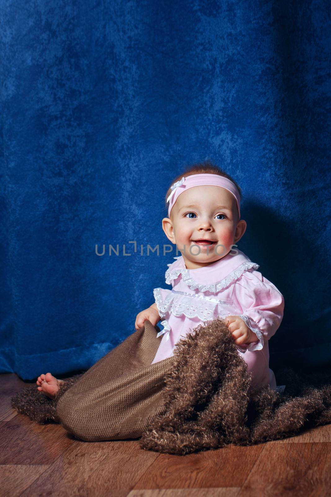 Pretty blue-eyed girl in a pink dress sitting on the floor