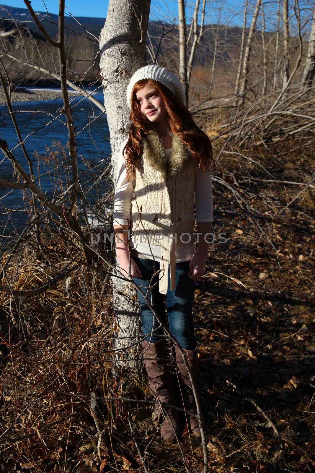 Winter girl leaning against a tree with river in the background 