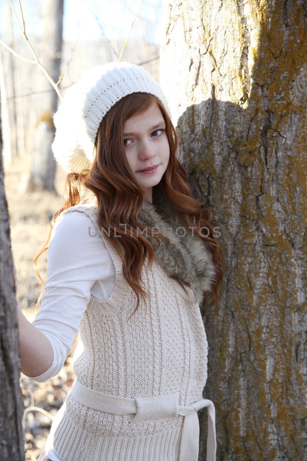Winter girl leaning against a large tree 