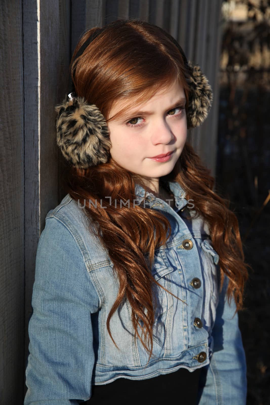 Red haired girl wearing earmuffs against wooden background 