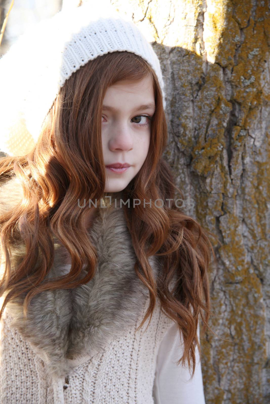 Winter girl leaning against a large tree 
