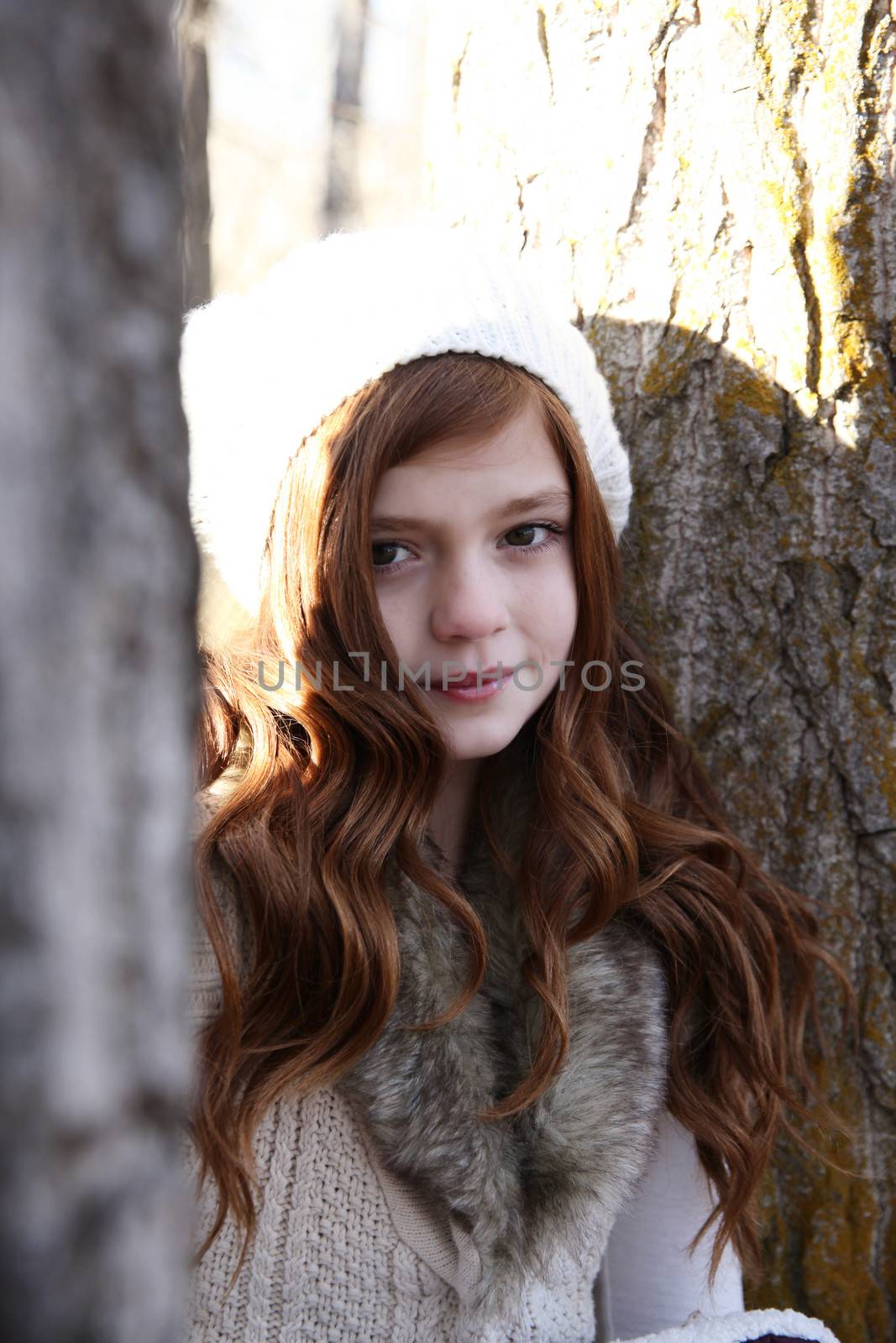 Winter girl leaning against a large tree 