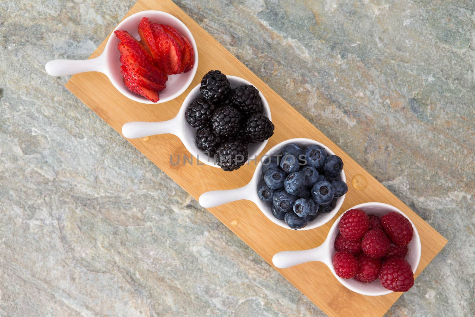 Dishes of fresh berries arranged diagonally on a small wooden board on a stone kitchen counter with copyspace ready for tasting and sampling these healthy autumn fruits