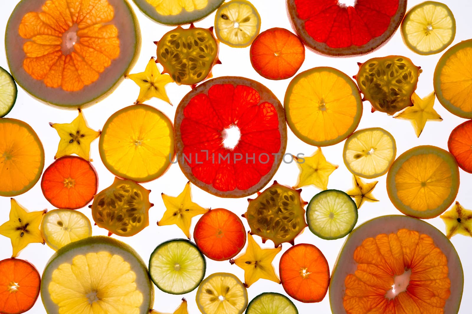 Vibrant background of translucent sliced fresh fruit neatly arranged on a white background with a variety of citrus, carambola or star fruit and kiwano or horned melon