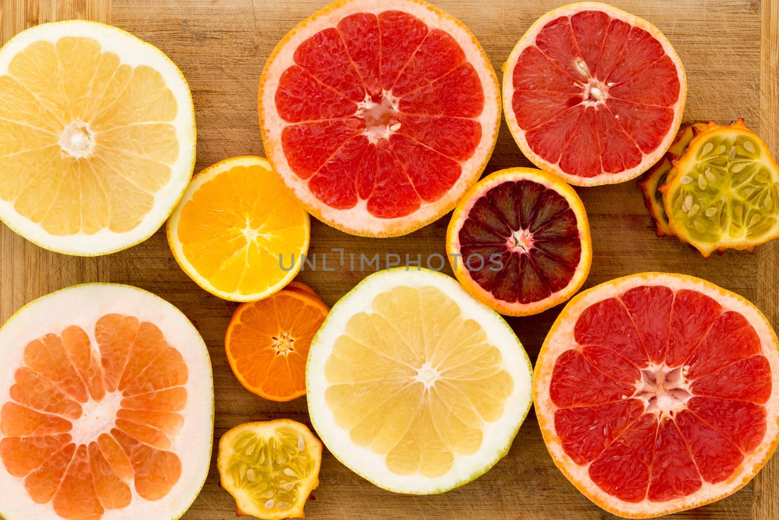 Colorful festive assortment of halved citrus fruit arranged on a wooden board with a variety of grapefruit, orange, pomelo and kiwano or horned melon viewed from above