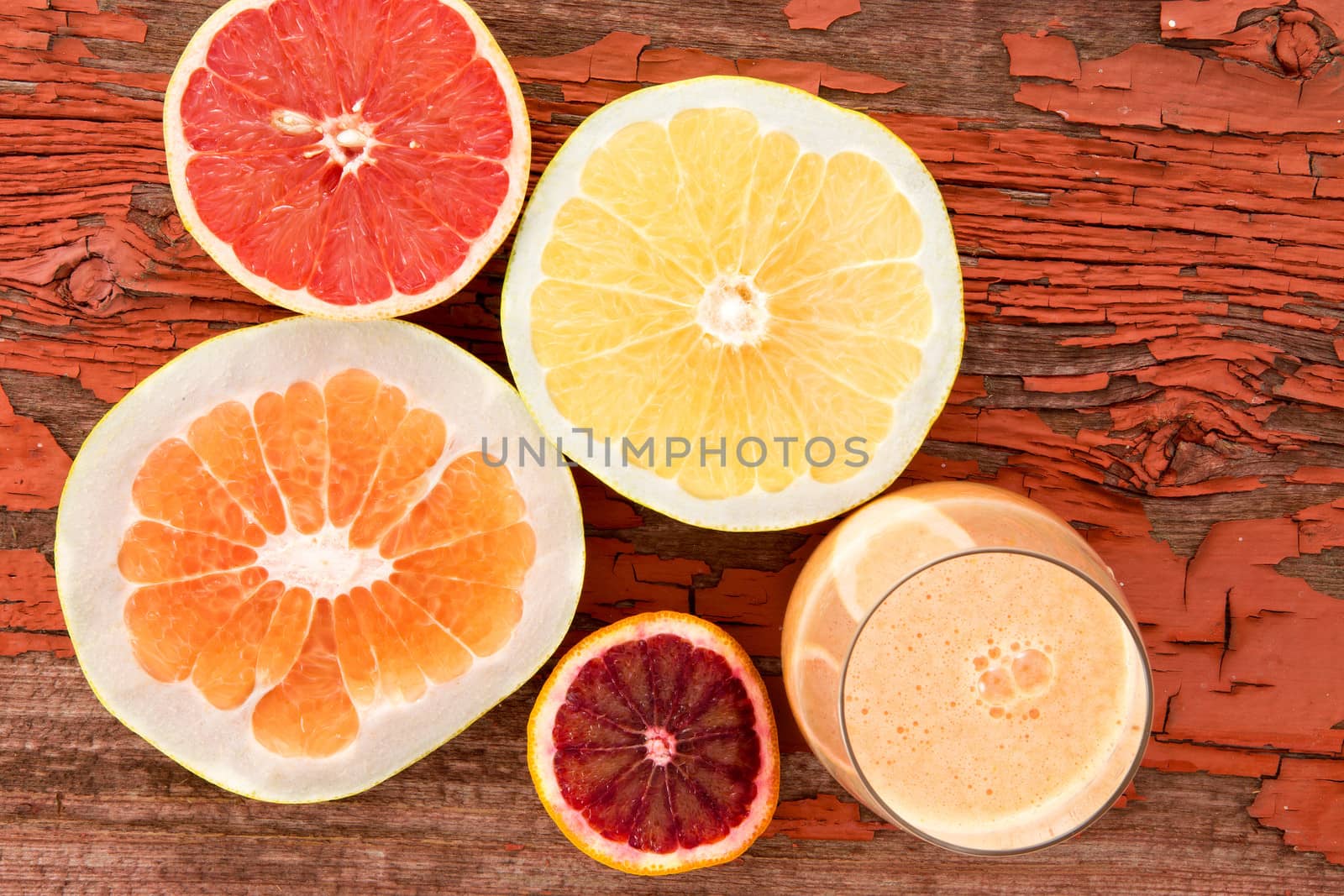 Glass of freshly liquidised grapefruit juice with halved fresh grapefruit, pomelo and ruby grapefruit on a grungy wooden background with red peeling paint and copyspace, overhead view