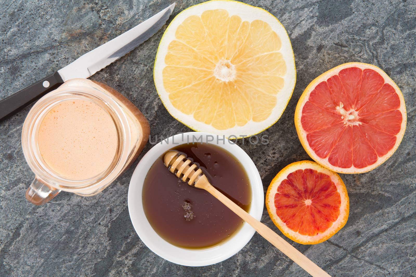 Delicious refreshing breakfast beverage of freshly squeezed grapefruit juice served with honey and grapefruit halves for a healthy breakfast, overhead view on a stone countertop