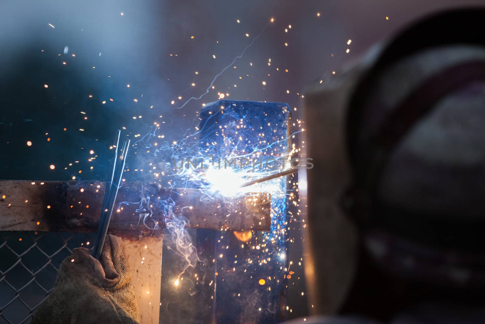 Heavy industry welder worker in protective mask hand holding arc welding torch working on metal construction