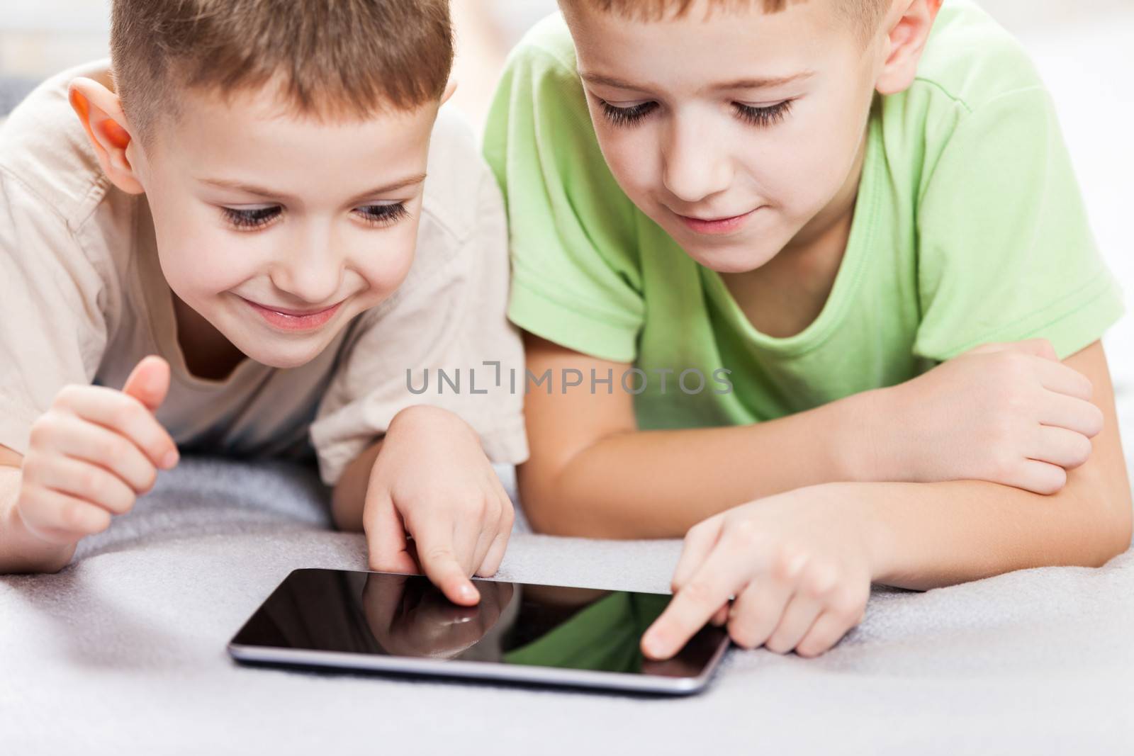 Two little smiling child boy brothers playing games or surfing internet on digital tablet computer