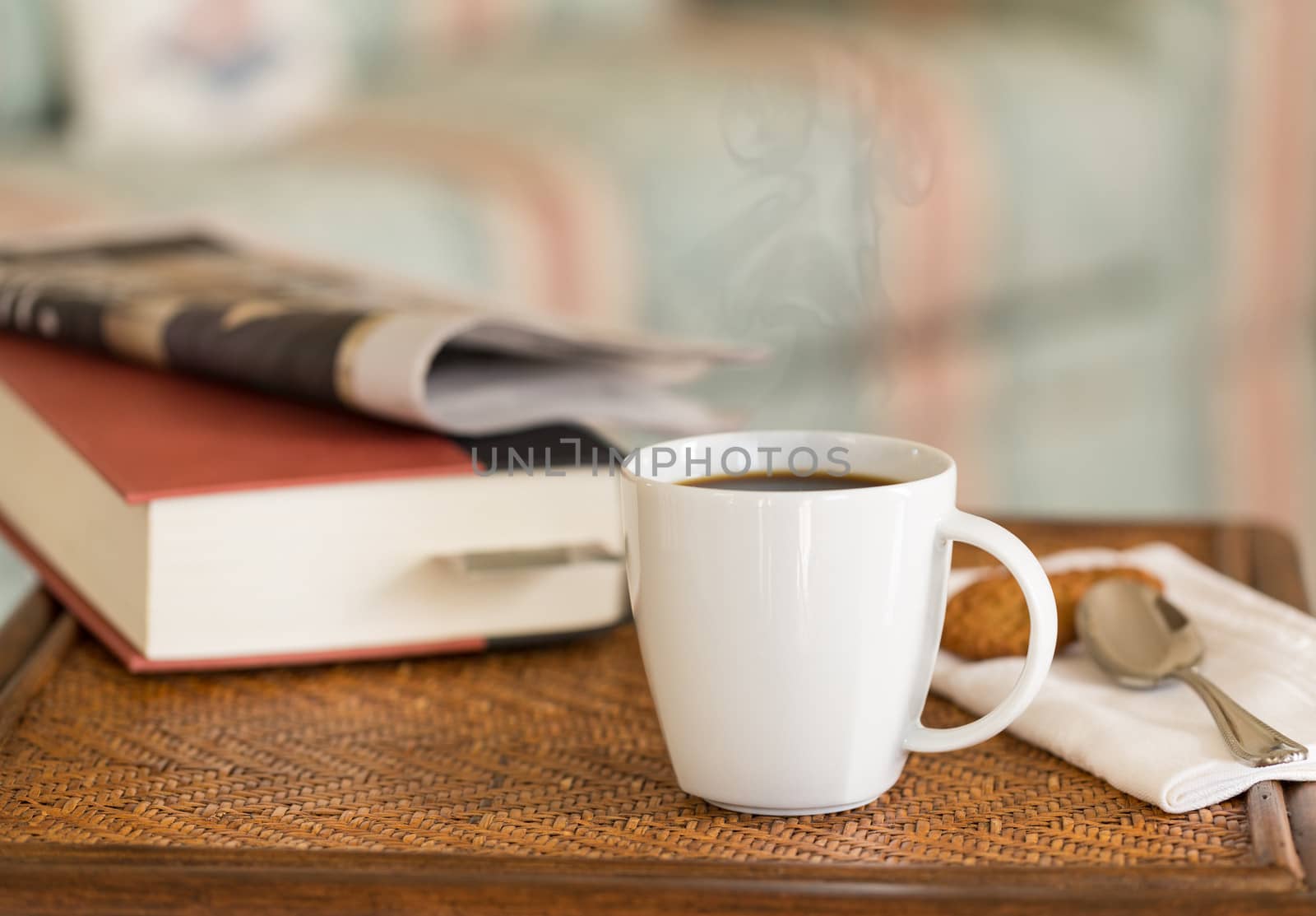 Modern white porcelain cup of black coffee on wooden wicker table with spoon and ginger biscuits and book