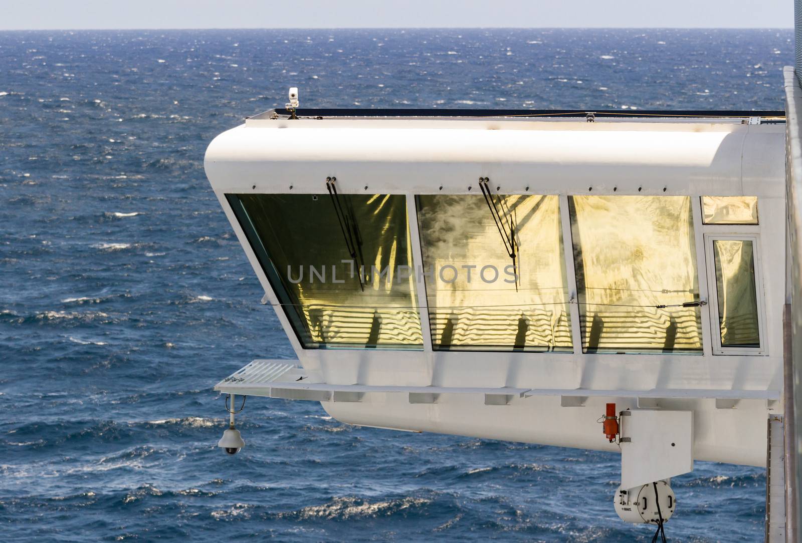 Cruise ship bridge cabin with the ships wake and surf reflected in the golden blinds on the windows as the ship sails to sea