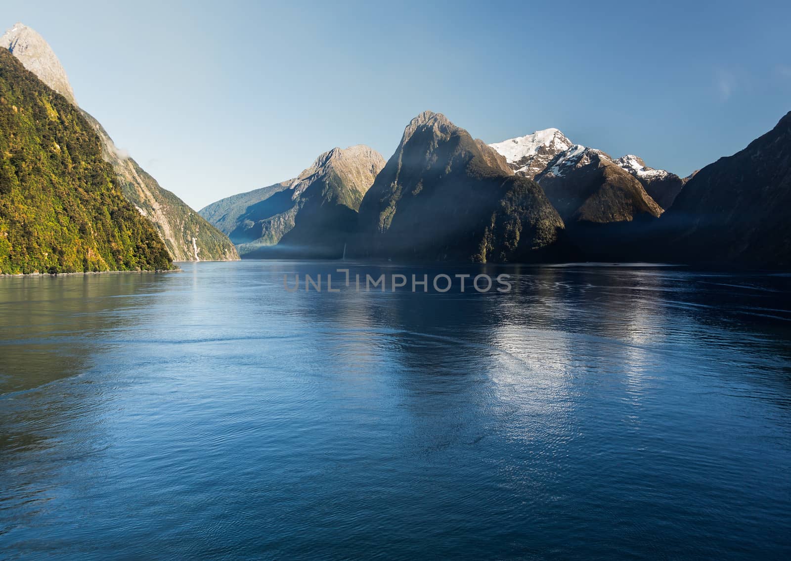 Sailing into Milford Sound on South Island of New Zealand in early morning as the sun rises above the mountains