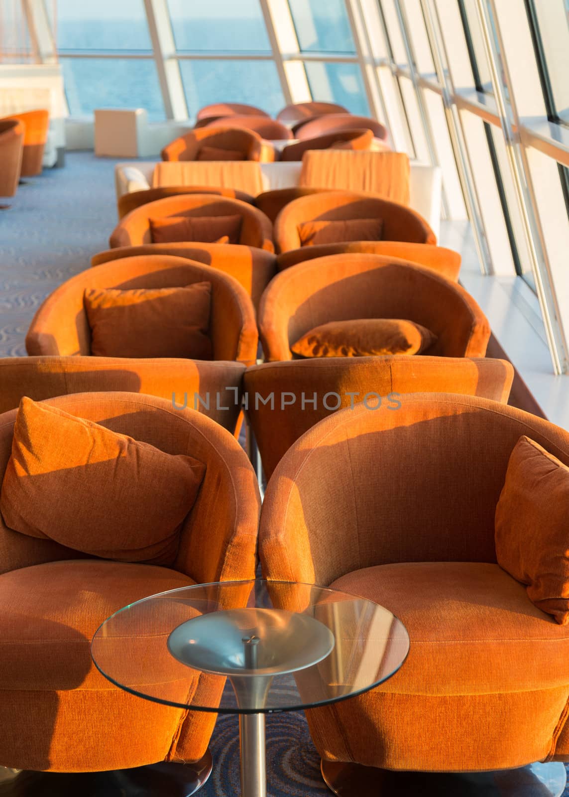 Row of cushioned seats or chairs and towel by high glass window looking out to sea with horizon in the distance